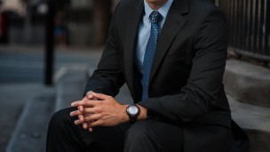 A man in a black suit sits on the steps of a building